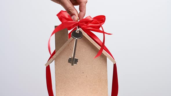 hand holds a metal key with a red ribbon on the background of a model house