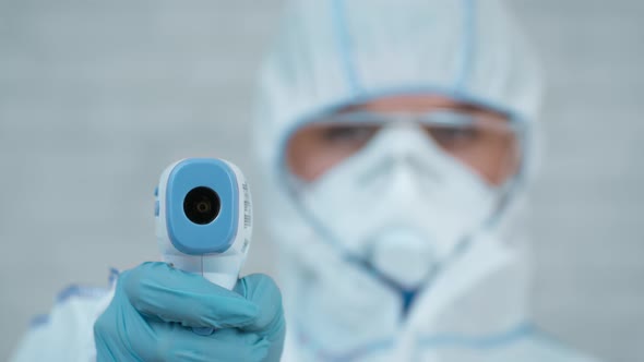 Medical Worker Doing Temperature Screening Pointing Thermometer To Camera Indoor