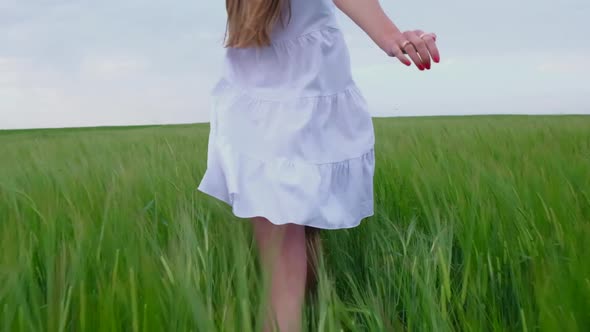 Girl in a White Dress Runs Across a Green Wheat Field