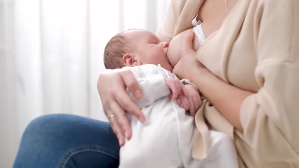 Young Caring Mother Sitting on Bed and Feeding Her Newborn Baby Boy with Breast Milk