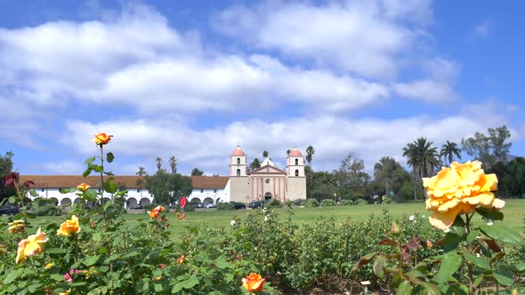 Reveal shot of the Santa Barbara Mission church building under blue and cloudy skies with flowers in