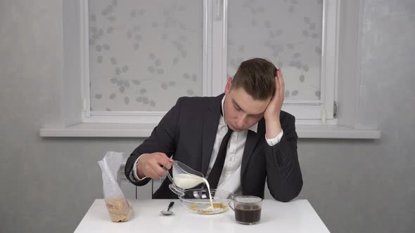 A Sleepy Young Man in a Suit Eats Cereal and Drinks Coffee