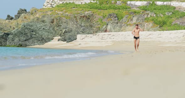 The Handsome Man with a Perfect Athletic Body in Swimming Trunks Having Fun on a Deserted Beach in