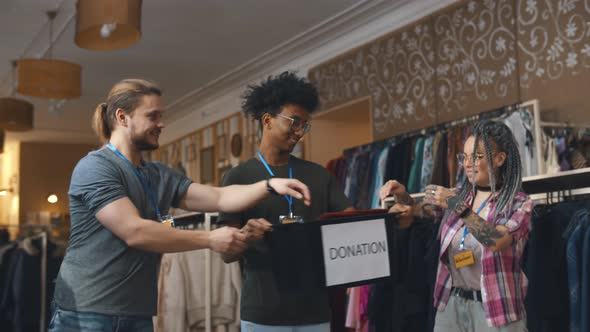 Diverse Young Volunteers Moving Donation Boxes with Clothes in Charity Shop