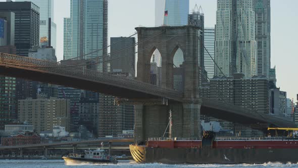 Cargo ship and boat floating under Brooklyn Bridge