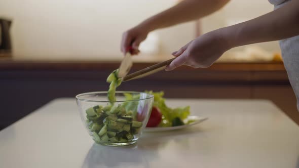 Woman Puts Cucumber Slices Into Glass Bowl on Table