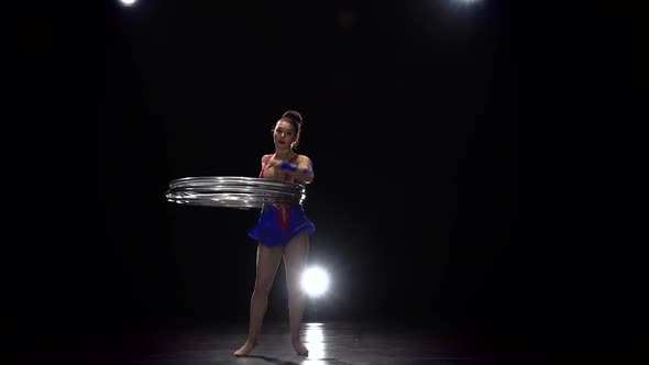 Gymnast in a Bright Outfit Twists a Hoop on Her Arm and Then on Her Leg