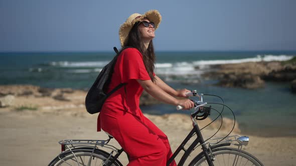 Tracking Shot Side View of Smiling Young Woman Riding Bicycle at Background of Mediterranean Sea