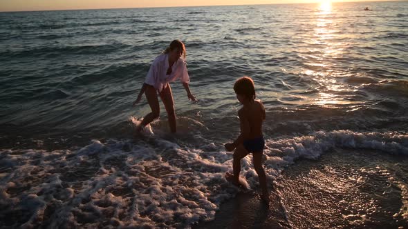 Young Woman and Her Son Come to Water on Sunset at Sandy Beach Island Holidays