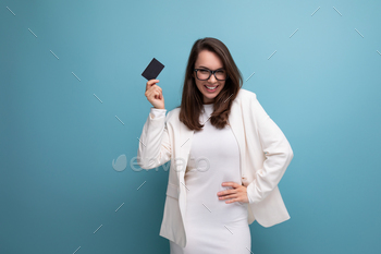 rich young woman with dark hair in a white dress holds a money card for payment