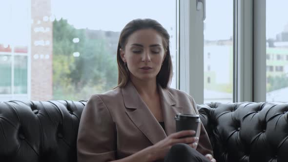 Young Girl Drinking Coffee on A break from Work, Sitting on the Couch in the Office