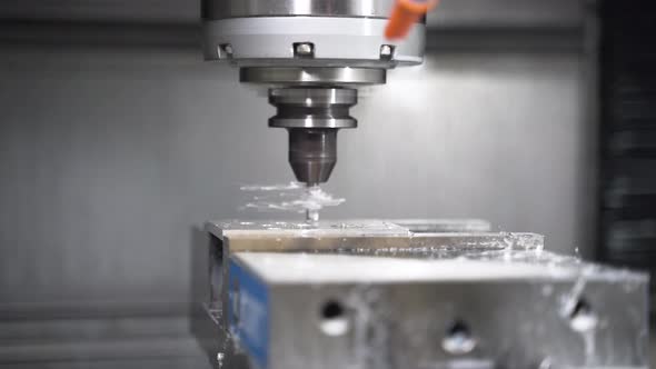 CNC machine drilling a hole in a metal plate, leaving metal splinters.