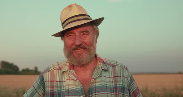 Portrait of Happy Senior Farmer in Hat Smiling at Camera in Sunny Field