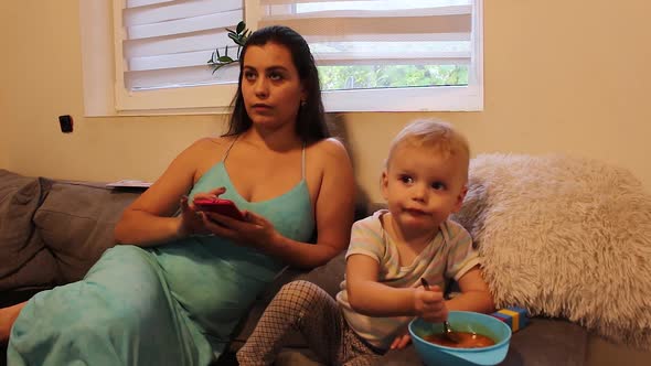 Little daughter eating soup while sitting with mother