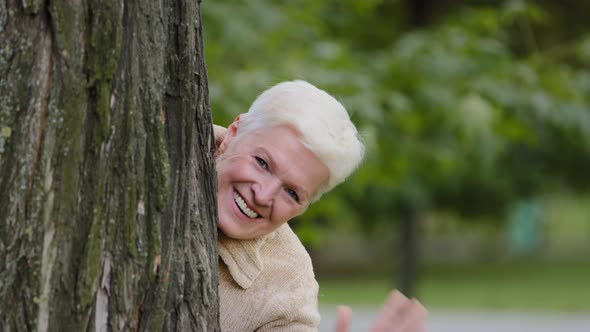 Funny Cheerful Mature Middle Aged Woman Hiding Behind Tree Plays Having Fun Peeping Out Waving Hand