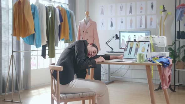Back View Of Asian Female Designer In Business Suit Yawning And Sleeping While Designing Clothes