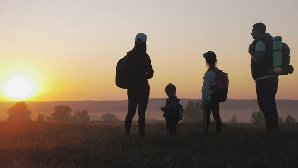 Silhouettes of Father, Mother and Children Hiking. Baby Sits on the Shoulders of His Father. Hiking