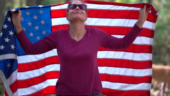 Blonde woman raising an American flag behind her with smiling expression and wrapping the flag aroun