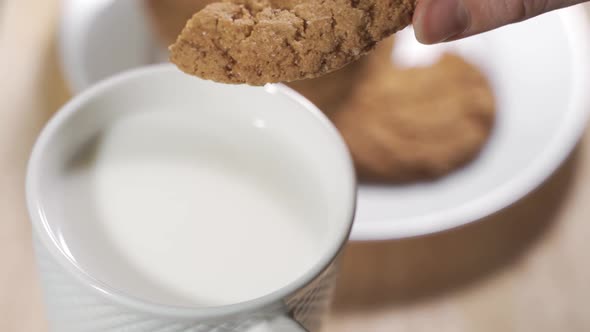 A Woman Hand Dunks a Cookie in the Milk Mug During the Breakfast in a Warm Morning.