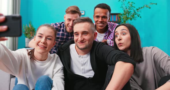 Joyous Multiethnic Group of Friends Sitting on Couch Together and Taking Selfie with Smartphone