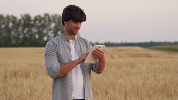 Man Farmer Using Digital Tablet Computer Standing in a Wheat Field and Using Apps and Checking