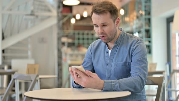 Upset Casual Man Having Loss on Smartphone in Cafe 