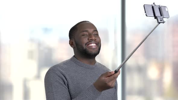 Smiling Man with Selfie Stick on Blurred Background.