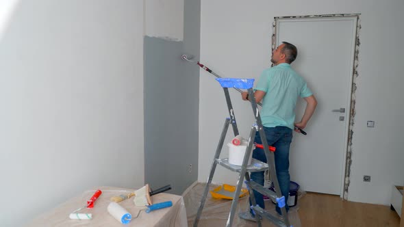 A Man Uses a Paint Roller to Paint the Wall Gray
