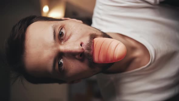 Man Chews and Spits Out a Children's Rubber Toy Bread and Looks Into the Camera