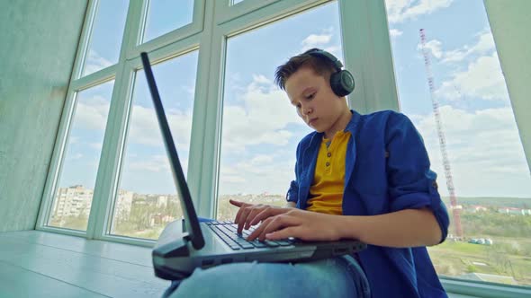 Teenager in headphones with a laptop by the window. 