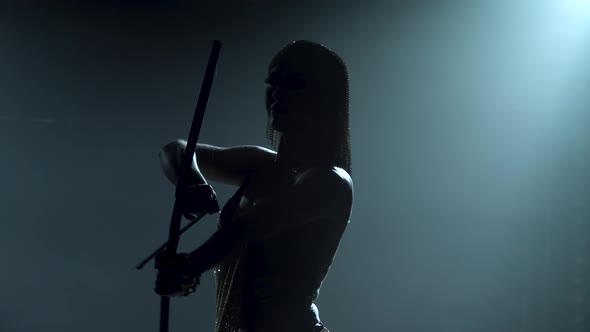 Silhouette of Joan of Arc with Bow and Arrow on Stage in a Dark Studio with Smoke and Neon Lighting