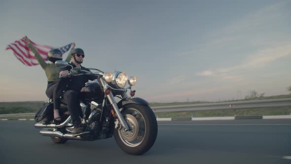 Couple Rides Motorbike on Highway Through the Desert Woman Holding Flag Waving in the Wind Side View