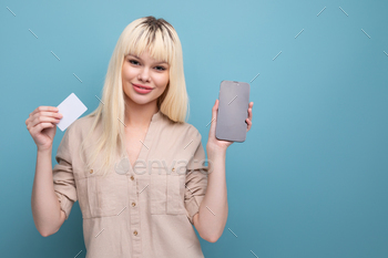 blondie young woman in casual clothes pays for the purchase using a smartphone and a money card