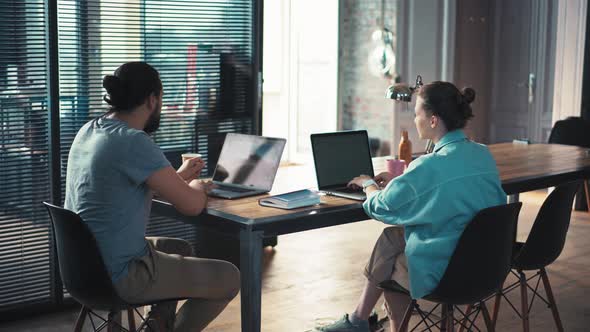 Two Coworkers are Discussing a Project While Sitting in Front of Their Laptops