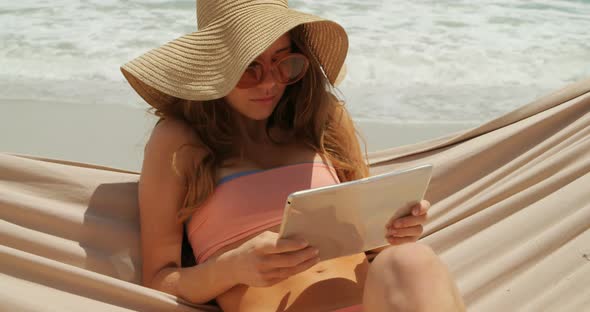 Front view of Caucasian woman using digital tablet in a hammock at beach 4k