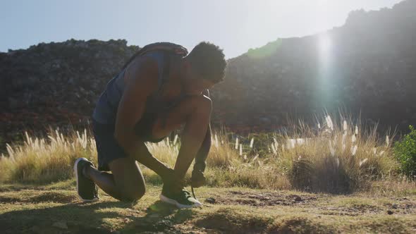 African american man exercising outdoors tying his shoe in countryside on a mountain