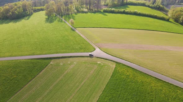 Car driving around a bend on an open country road through beautiful, lush green fields in the rural