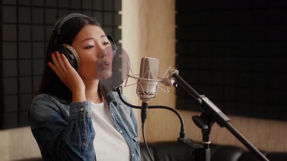 Talented Asian Female Singer Wearing Headphones Singing Song To Mic In Studio