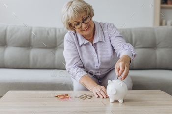 people concept – smiling senior woman putting coins into piggy bank at home