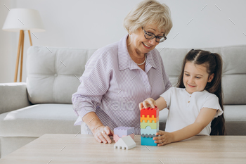 Grandmother playing a board game with granddaughter, sitting in the living room together