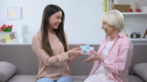 Beautiful Young Lady Presenting Gift Box to Grandmother, Birthday Celebration