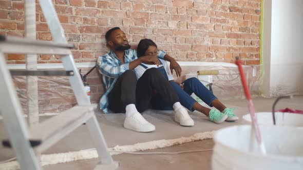 Happy Young African Couple Relaxing After Painting Room in New House on Floor.