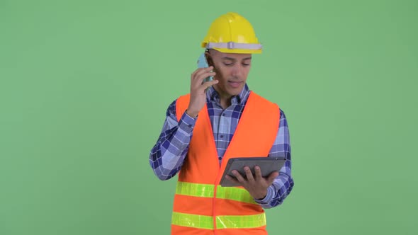Happy Multi Ethnic Man Construction Worker Talking on the Phone While Using Digital Tablet