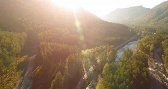 Mid Air Flight Over Fresh Mountain River and Meadow at Sunny Summer Morning. Rural Dirt Road Below.