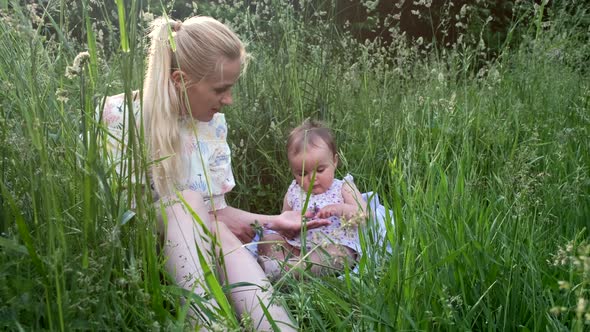 A young mother with a little daughter plays among the grass.