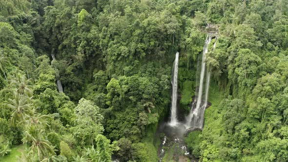 Slow drawing back tracking shot of tall lush jungle waterfall