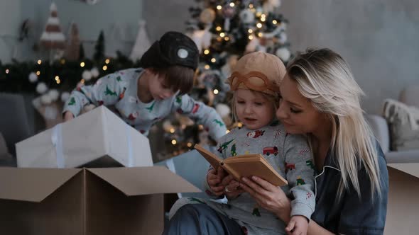 Young Family with Two Small Children Reading a Book for Christmas Happy Woman with Sons on Winter