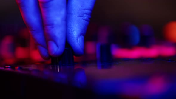 Closeup of DJs Hands Twisting Knobs on Mixing Console Adjusting Volume of Music in Nightclub Disco