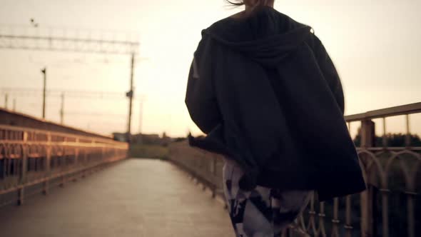 View From Back Young Girl with Tied Hair Running Along City Bridge at Sunset in Slow Motion