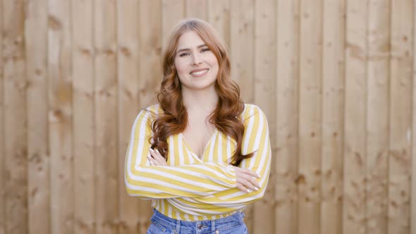 Confident woman standing in front of wooden wall with arms crossed